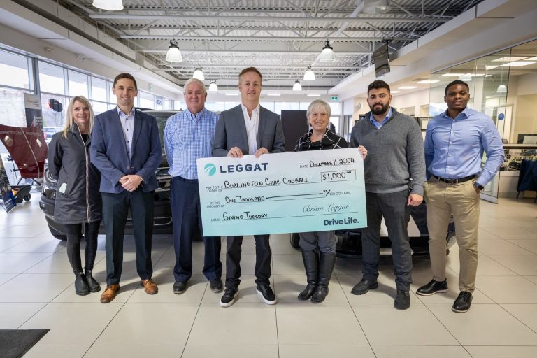 A photo of people holding a large cheque that is being donated to Burlington Civic Chorale from Leggat for $1,000.